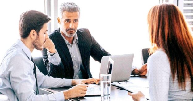 Gruppo di persone in riunione sedute al tavolo che discutono con finestra di sfondo